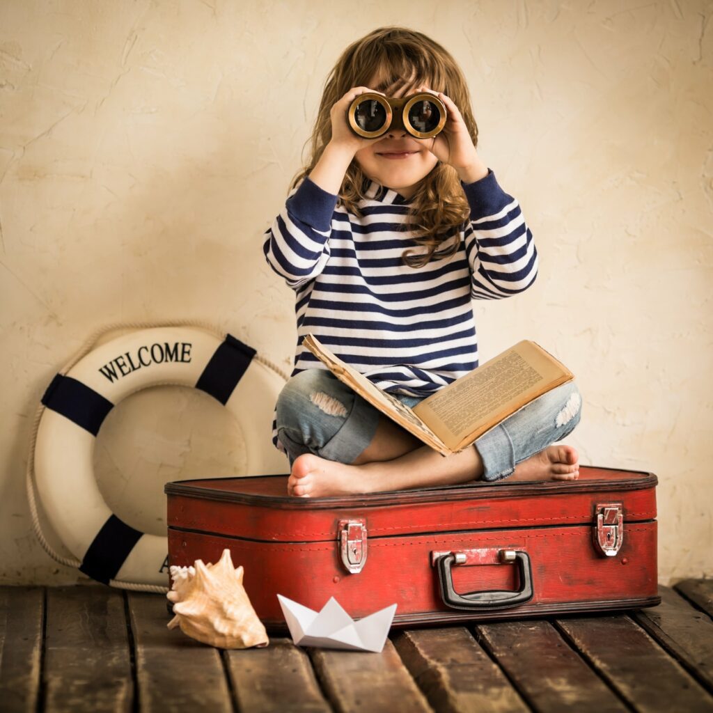 Happy kid playing with toy sailing boat indoors. Travel and adventure concept