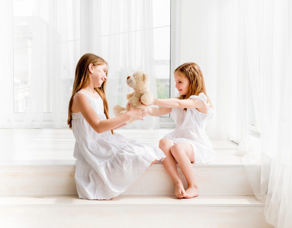 Little girl giving her teddy bear toy to older sister. Cute child girl giving a gift for her sister. Child girl sharing toy with friend